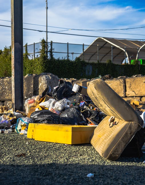 A close-up view of a black plastic rubbish bag tied securely at the top, positioned in the foreground with another similar bag partially visible behind it. The bags appear to be filled with waste, wit